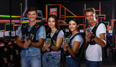 Smiling young people with laser guns having fun together in dark labyrinth