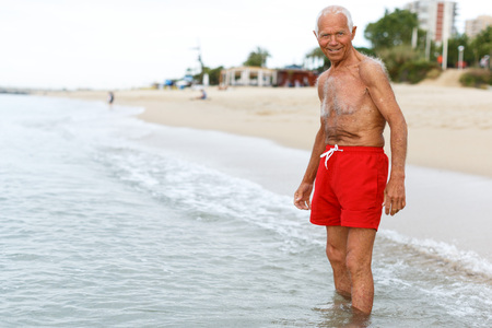 Nice mature man checks the water temperature on the beachの写真素材