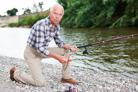 Portrait of mature man standing and fishing at river beach on summer dayの写真素材