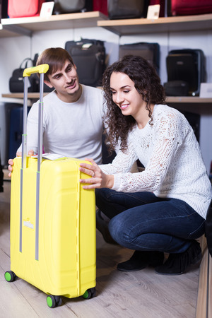 Positive adult customers looking at roll-aboard bags in storeの写真素材