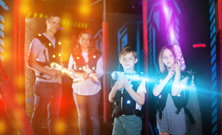 Portrait of excited kids in bright beams of laser guns during laser tag game in dark room with parentsの写真素材