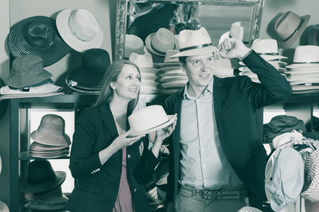 smiling young female and man choosing hats from the assortment in the storeの写真素材