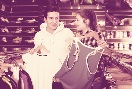 Young cheerful positive female with male are choosing new T-shirt for tennis for him in the speciality store.の写真素材