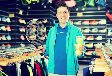 Tennis male is standing in uniform with new tennis rocket and balls in the speciality storeの写真素材