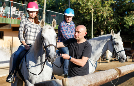 Portrait of mature couple with trainer riding horse at farm outdoorの写真素材