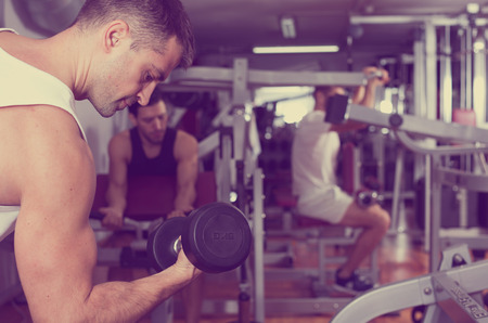 Concentrated sporty guy during workout in gym with dumbbellsの写真素材