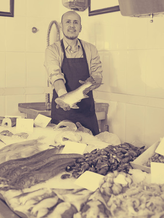Senior man selling frozen fish and seafood in storeの写真素材