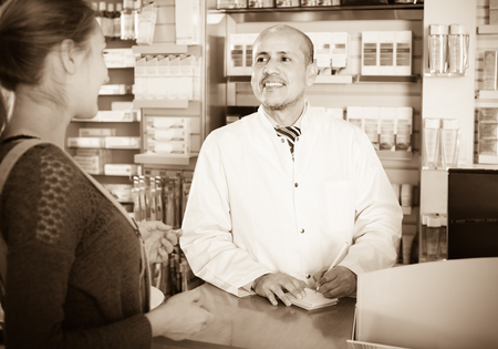 Friendly smiling male pharmacist serving young woman in pharmacyの写真素材