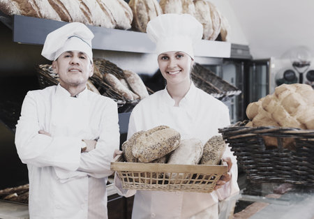 Male and female bakers 30-35 years old are with tasty and fresh bread products on counter.