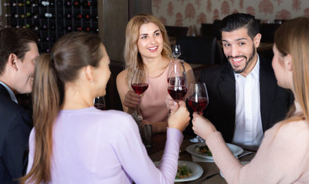 Ð¡heerful  smiling friends having dinner and drinking red wine in restaurant