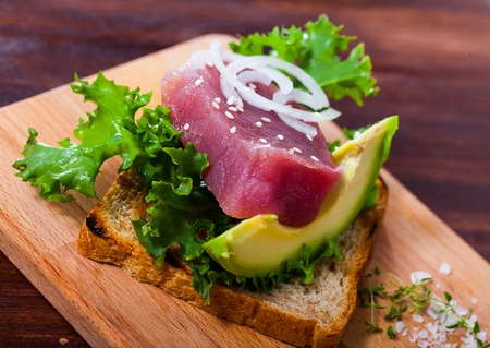 Toasted bread with raw tuna steak, salad, avocado and onion ringsの写真素材