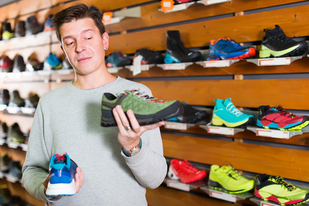 Young attractive athlete chooses sporty clothes and comfortable shoes from assortment in the sports shopの写真素材