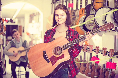happy american  teenage customers deciding on suitable acoustic guitar in guitar shopの写真素材