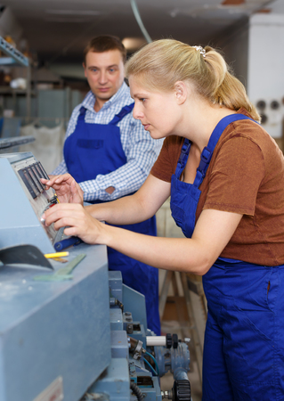 Young woman with male assistant working on glass beveling machine in workshopの写真素材