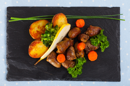 Top view of fried chicken hearts with baked vegetables and fresh pear on black serving boardの写真素材