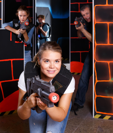 positive girl with laser pistol playing laser tag with friends on dark labyrinthの写真素材