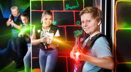 Portrait of teenager boy with laser gun having fun with family on a dark lasertag arenaの写真素材