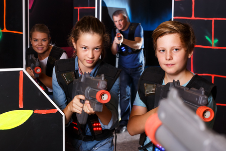 Smiling teenage boy and girl with laser guns having fun with adults on dark lasertag arenaの写真素材