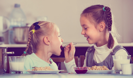 Portrait of  two cheerful little girls eating porridge with jam in kitchenの写真素材