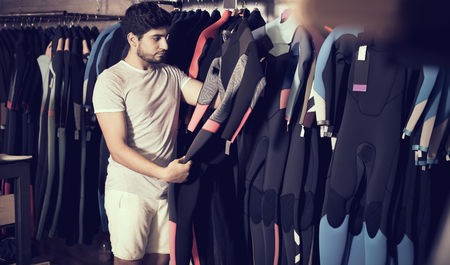 Adult european man holding and choosing suit for surfing in the shopの写真素材