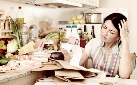 Woman is unpleasantly surprised of price in the check after shopping in grocery market at home.の写真素材
