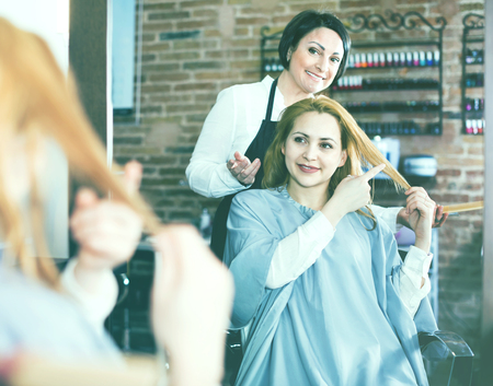 Young smiling  woman points to master in hairdress salon right hair length for haircutの写真素材