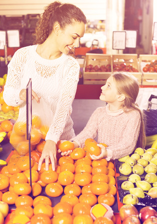 Happy positive smiling mother and little girl choosing fresh fruits in groceryの写真素材