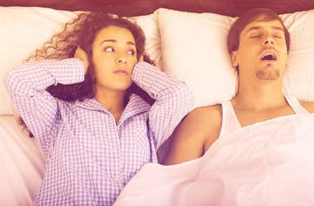 Boyfriend snorring and angry woman lying in bed awakeの写真素材