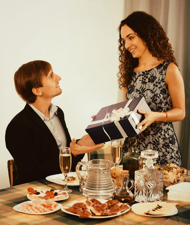 Woman giving present to happy man at tableの写真素材