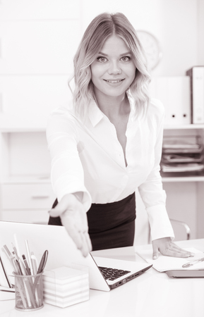 Kindly girl with an outstretched hand is standing near tableの写真素材