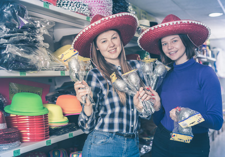 Portrait of two cheerful girls in sombrero with maracas in hands while preparing for party in festive things shopの写真素材