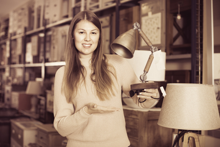 Portrait of cheerful  positive woman buyer choosing modern lamp in furniture shopの写真素材