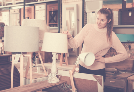 portrait of smiling young consumer choosing torchere in furniture shopping roomの写真素材