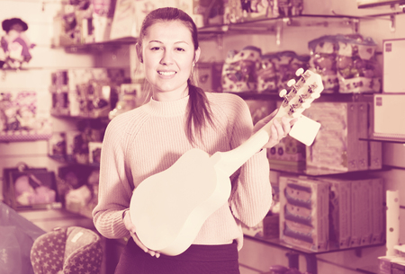 Smiling cheerful  female consumer holding toy guitar in the children's storeの写真素材