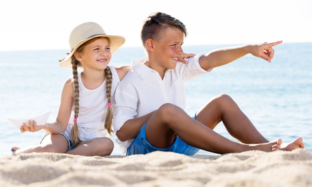 Portrait of beautiful boy and girl pointing with finger on sandy beach on bright weatherの写真素材