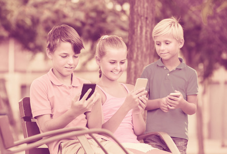 cheeful english kids are chatting in phones in the playground.の写真素材