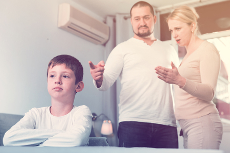 Portrait of upset boy scolded by parents at homeの写真素材