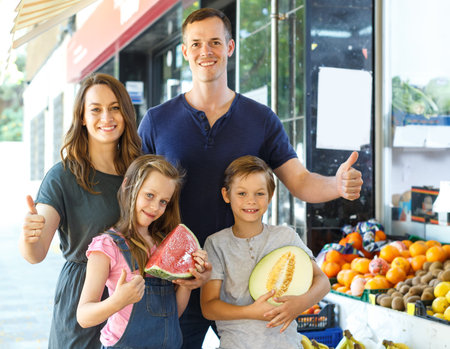 Happy family with children demostration fresh fruits  in local fruit store outdoor