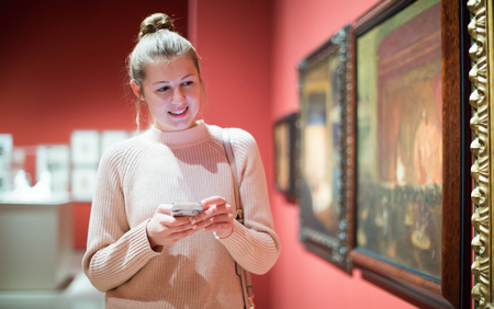 Positive woman visitor using  phone  in the historical museumの写真素材