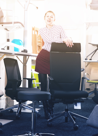 Stylish smiling girl standing among various chairs for sale in furniture shopの写真素材