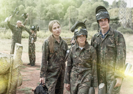 grieved young people lost paintball match, standing outdoors with protective mask with traces of paintの写真素材