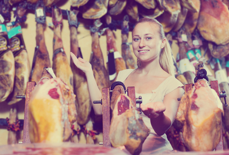 Beautiful young woman picking delicious prosciutto meat on marketの写真素材