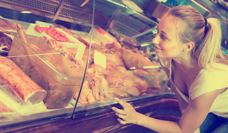 Smiling young woman customer buying fresh poultry parts in meat shopの写真素材