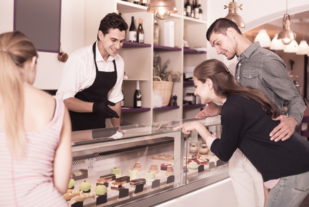 Positive seller helping friends to choose sweets in comfortable cafeの写真素材