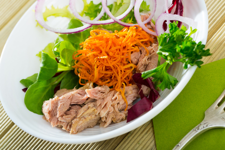 Fresh salad of grated carrots, canned fish, greens and onion in white bowlの写真素材