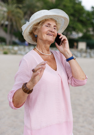 Smiling senior woman talking on phone during seaside walkの写真素材