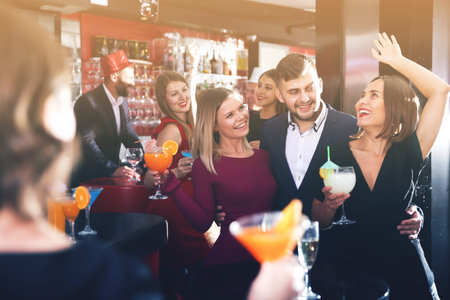 Cheerful guy with two girls partying in bar, dancing and toasting drinks