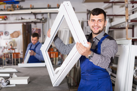 happy male professional labours with finished PVC profiles and windows at factoryの写真素材