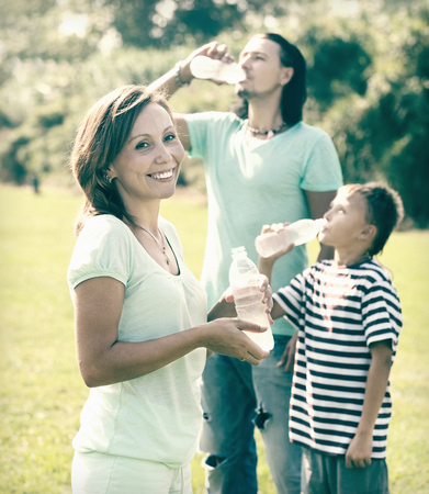 Happy ordinary  couple with teenager drinking water from plastic bottles in summerの写真素材
