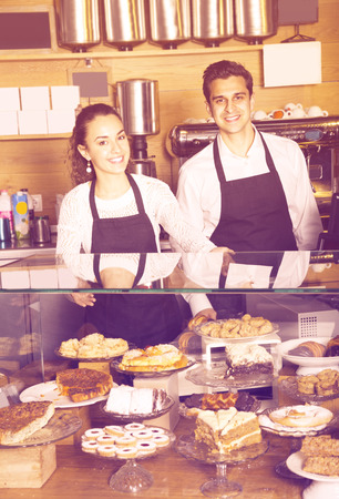 Smiling happy cooks selling tarts and sweet pastry in coffee-houseの写真素材